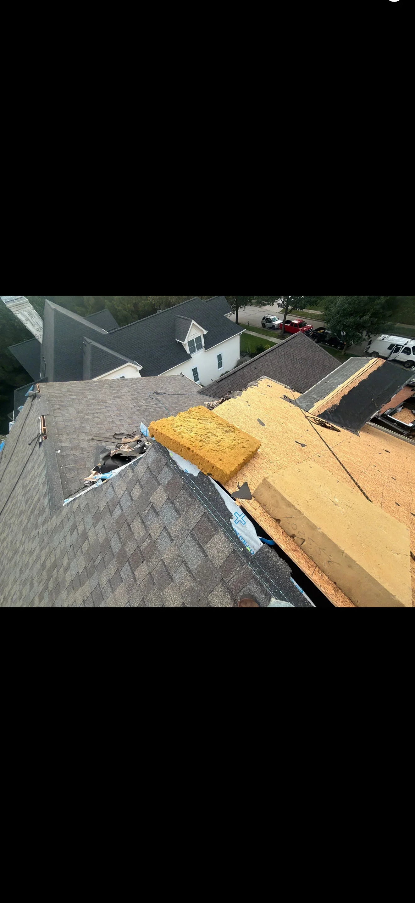 Partially stripped residential roof showing exposed plywood sheathing, torn underlayment, and remaining dark asphalt shingles