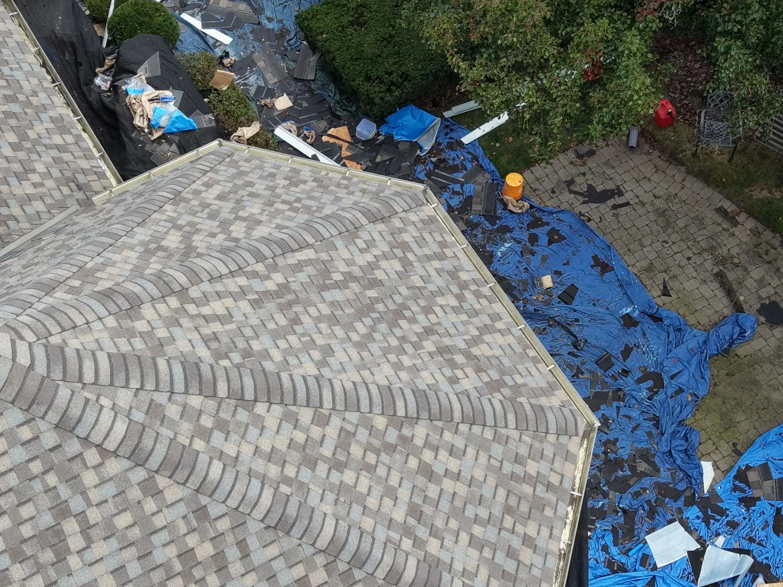 Aerial view of architectural asphalt shingle roof installation with old shingles torn off and tarped on the ground