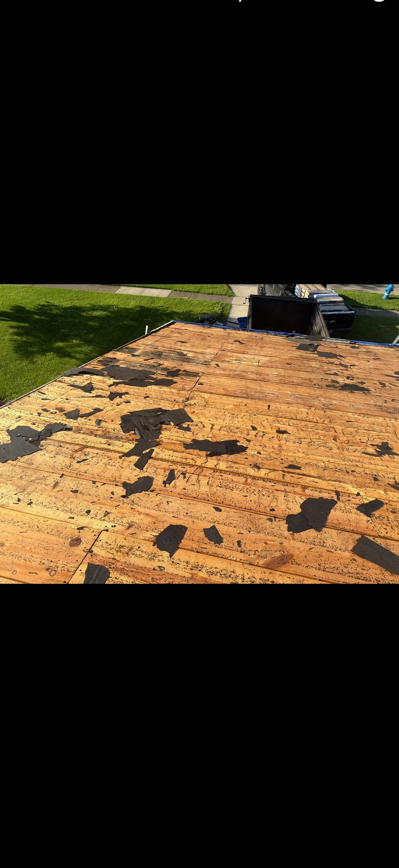 Bare roof deck with scattered remnants of black asphalt shingles during a tear-off, dumpster at eave