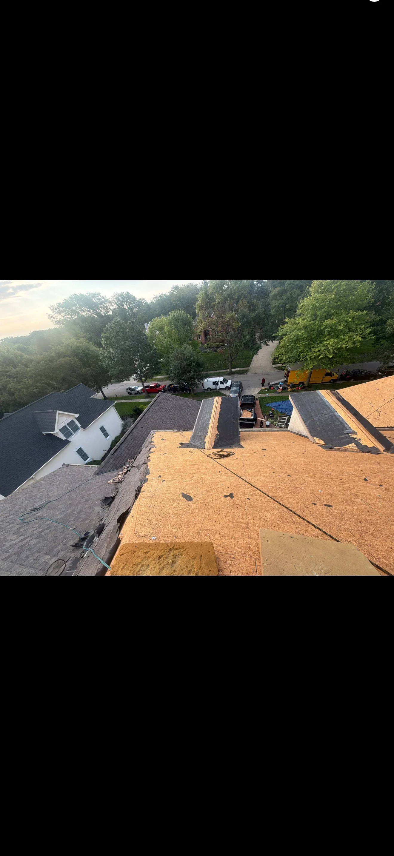 Roof tear-off in progress with exposed OSB sheathing, partially removed asphalt shingles, and dormers on a steep residential roof