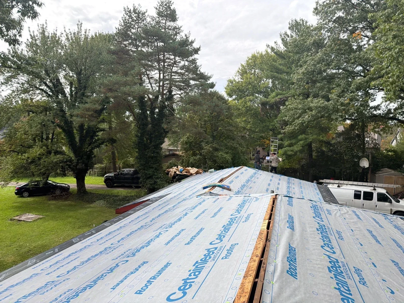 Synthetic CertainTeed RoofRunner underlayment installed over a sloped roof deck with wood sheathing and crew at ridge