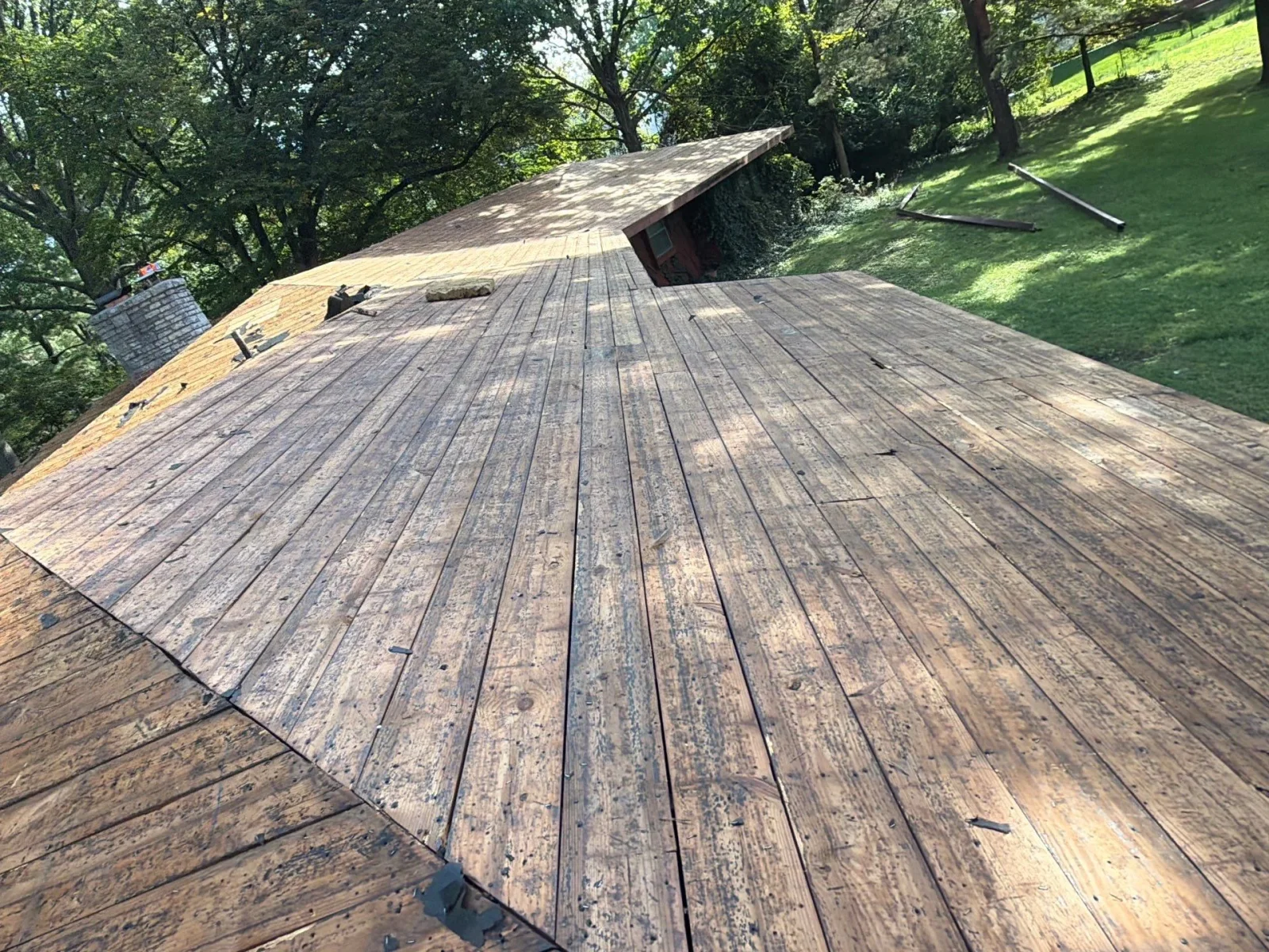 Exposed weathered wood plank roof decking during tear-off with OSB sheathing and stone chimney visible