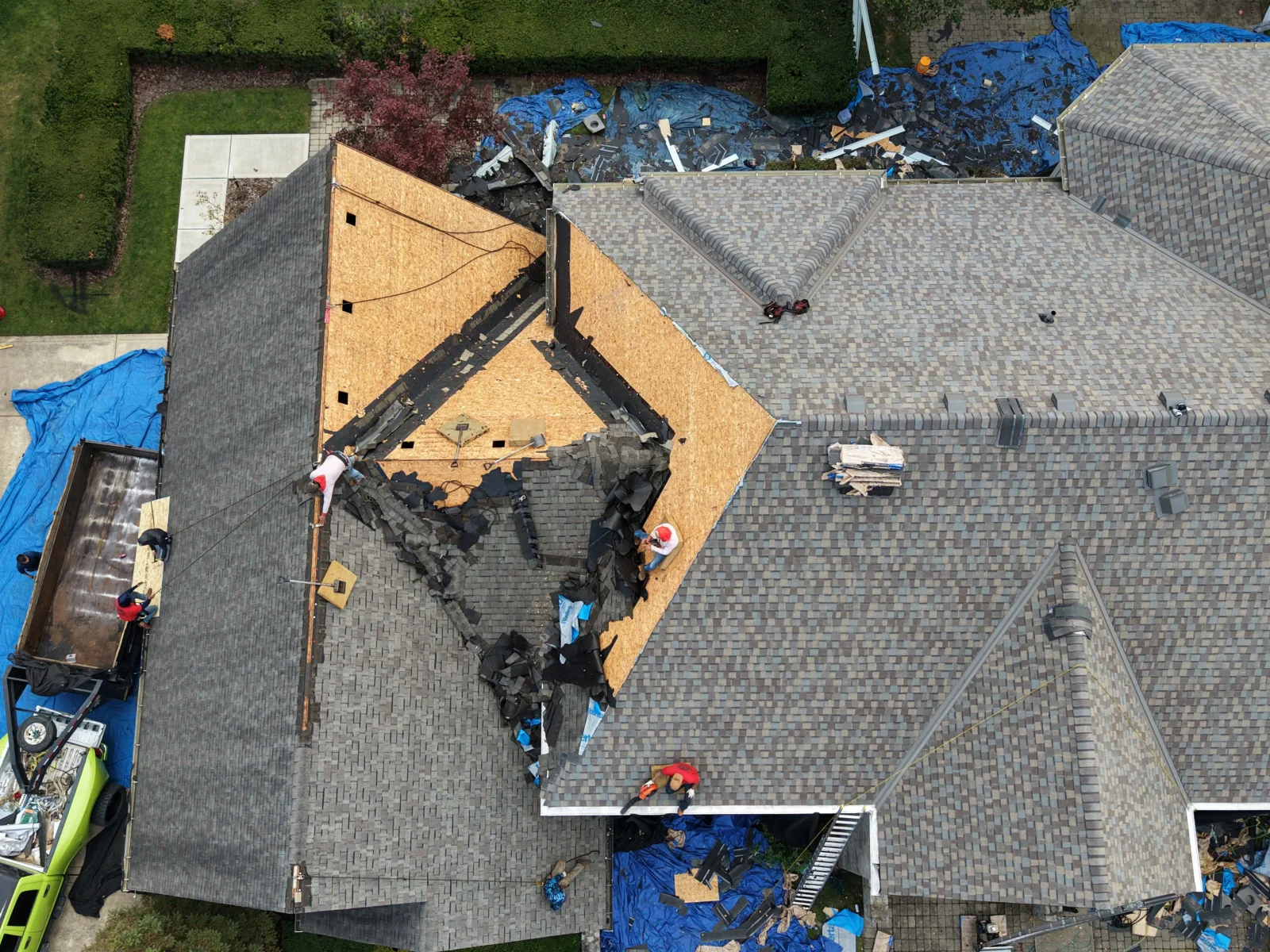 Aerial view of asphalt shingle roof tear-off exposing OSB decking, with crew working on sloped planes and debris dumpster