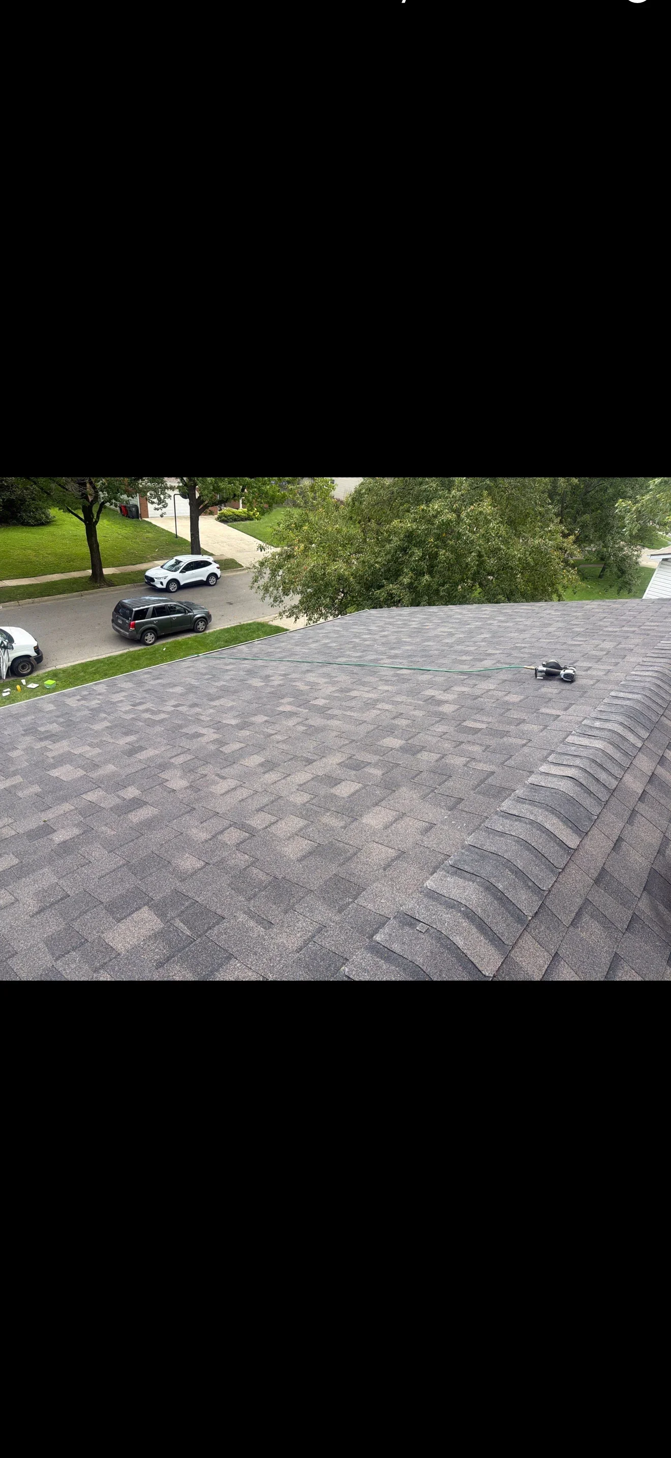 Architectural asphalt shingle roof in gray blend with ridge cap installation and pneumatic nailer on roof