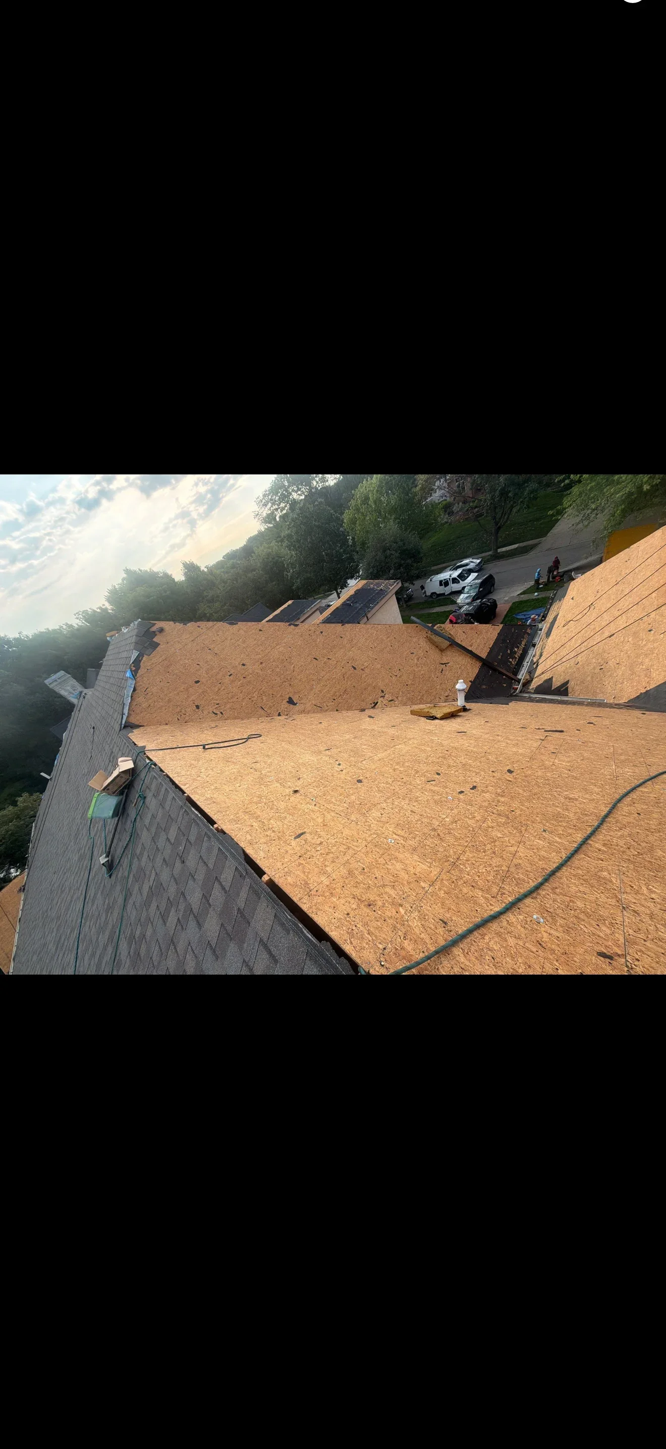 Steep roof mid tear-off showing exposed OSB sheathing, remaining asphalt shingles, and a plumbing vent pipe