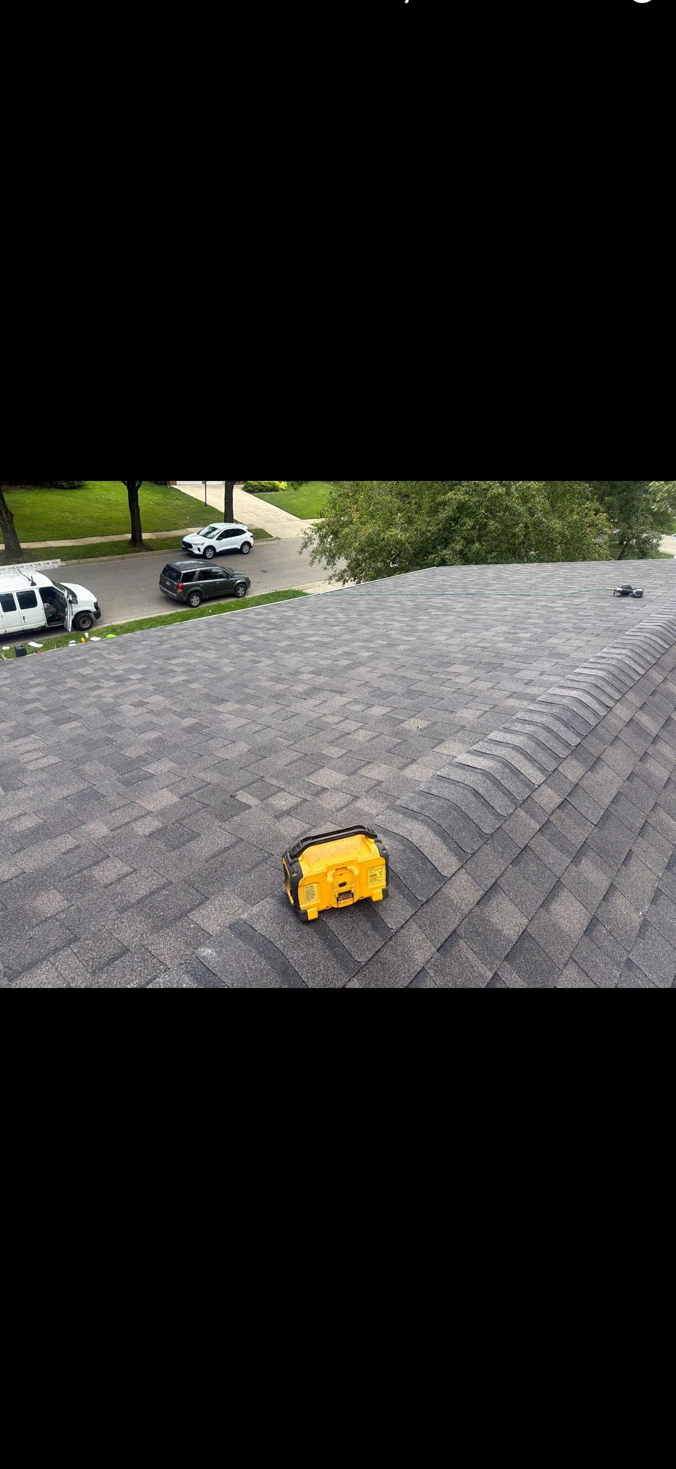 Gray architectural asphalt shingle roof with stepped ridge cap shingles and portable generator on roof surface