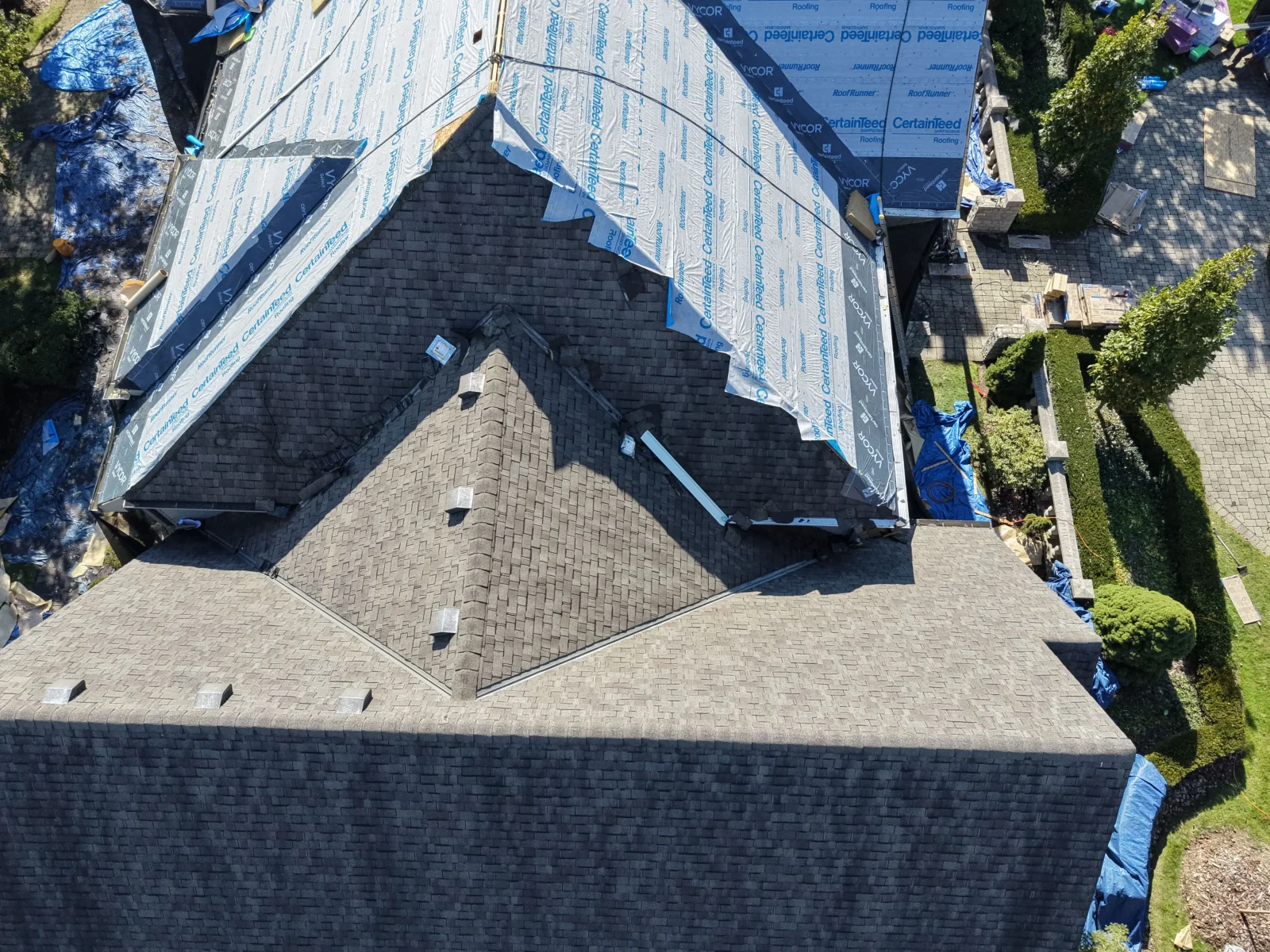 Aerial view of roof with CertainTeed RoofRunner synthetic underlayment, dark architectural shingles, and metal pipe vents during replacement