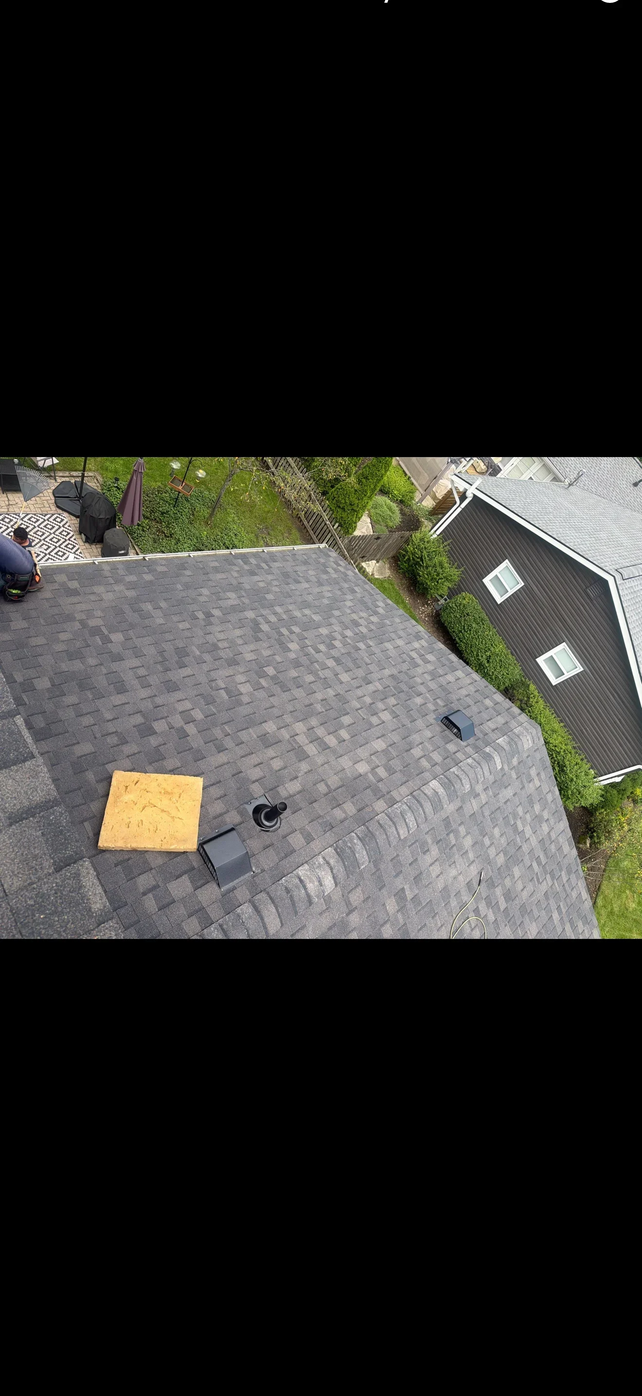 Dark gray architectural shingle roof with black box vents, plumbing vent pipe, and white gutter edge on a dark-sided home