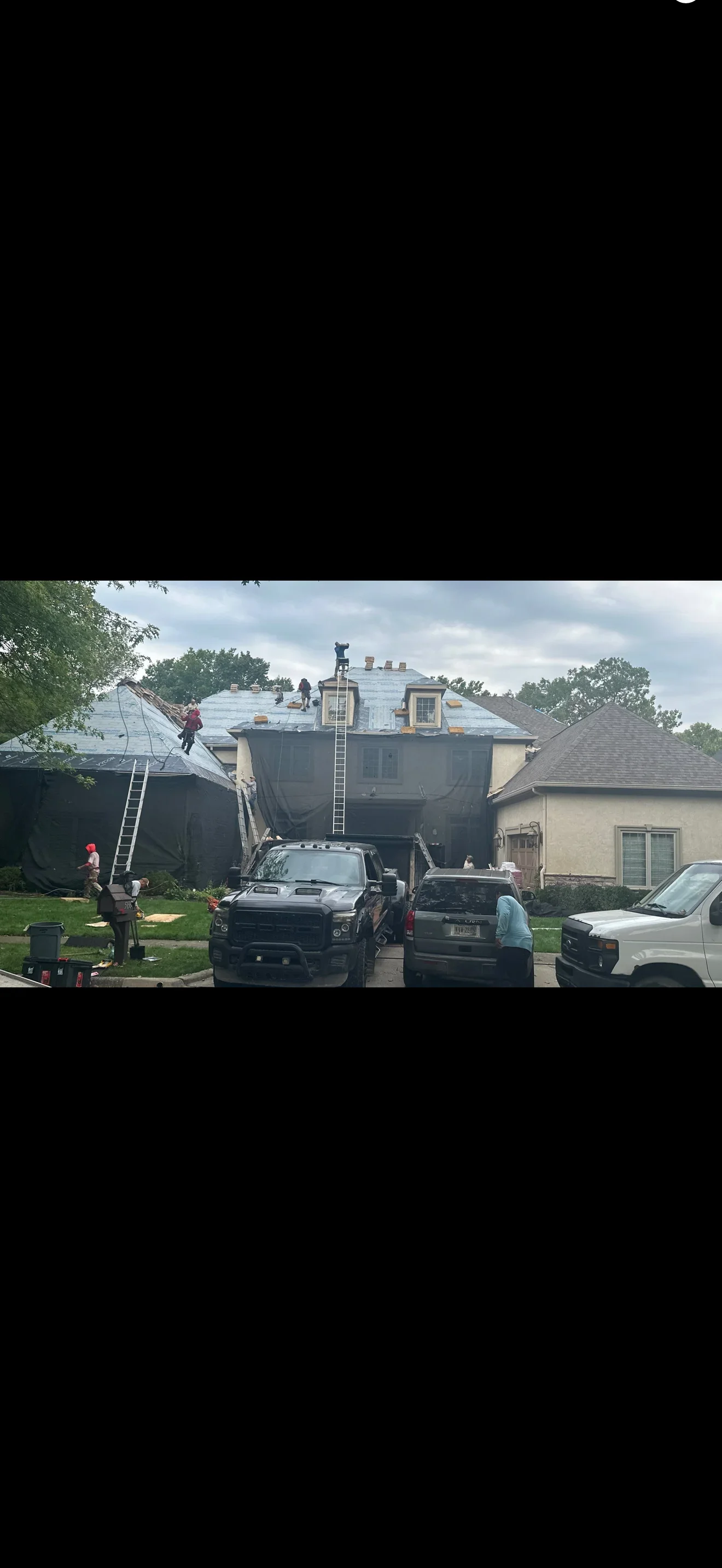 Crew tearing off shingles on a stucco home roof with dormers, ladders, and tarps protecting walls
