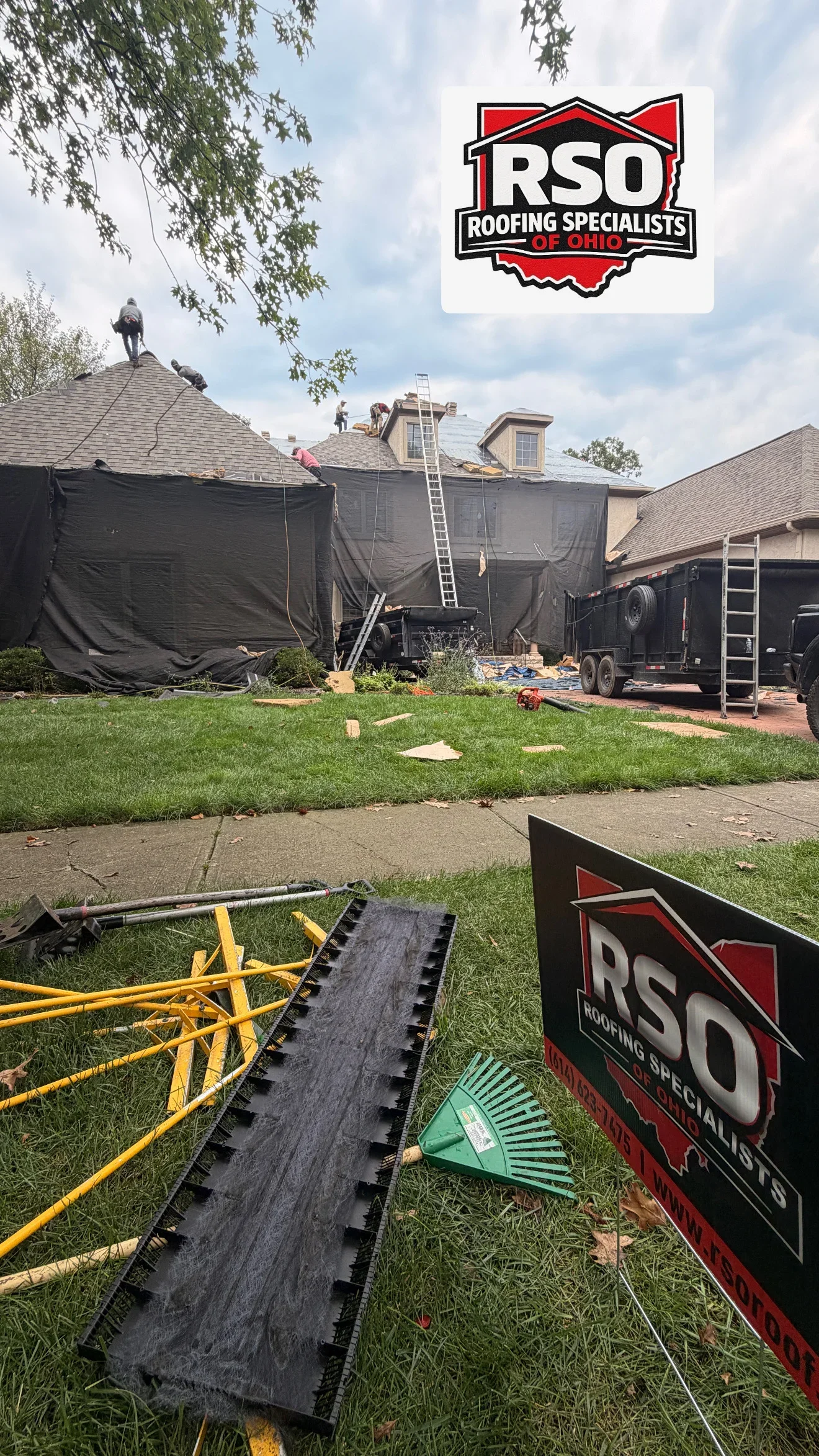 Crew performing roof tear-off on two-story home with asphalt shingles, black protective tarps, and metal extension ladder