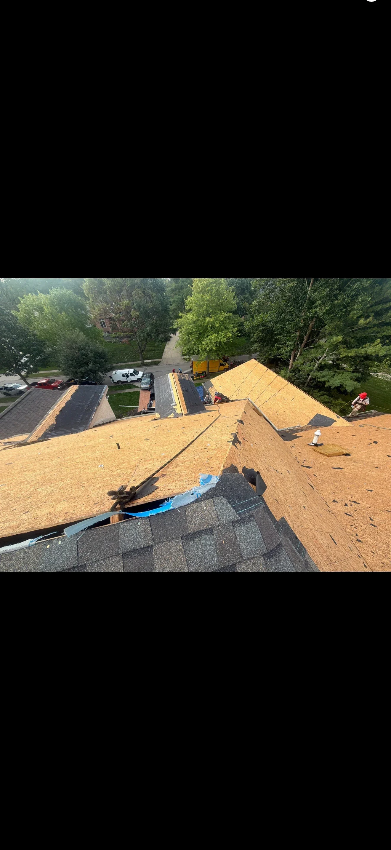Roof tear-off showing bare OSB sheathing, blue underlayment at valley, and asphalt shingles remaining at eave
