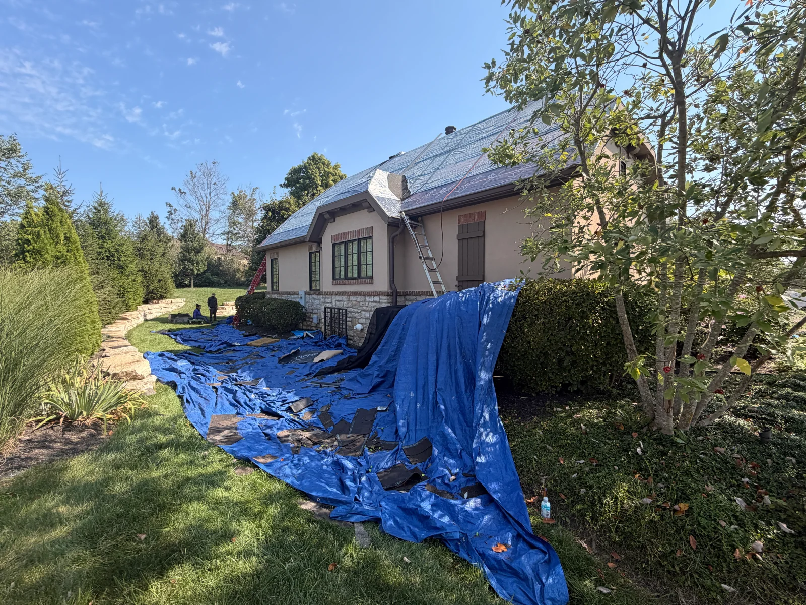 Steep stucco home roof being torn off with old shingles on blue tarp and underlayment installed on deck