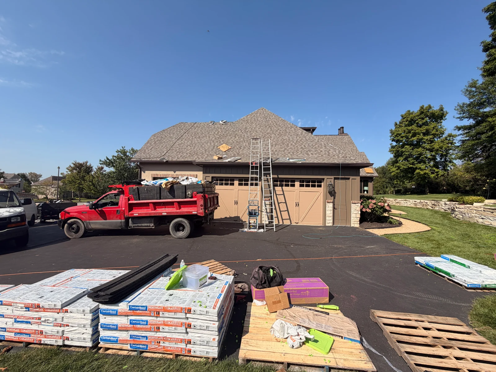 Asphalt shingle roof replacement in progress with CertainTeed NorthGate ClimateFlex bundles and ladders on driveway